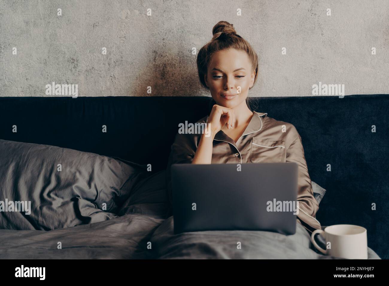 Positiva giovane donna rilassata che naviga su Internet per guardare il film preferito sul laptop mentre trascorre una giornata pigra a casa, sdraiata a letto a casa e looki Foto Stock