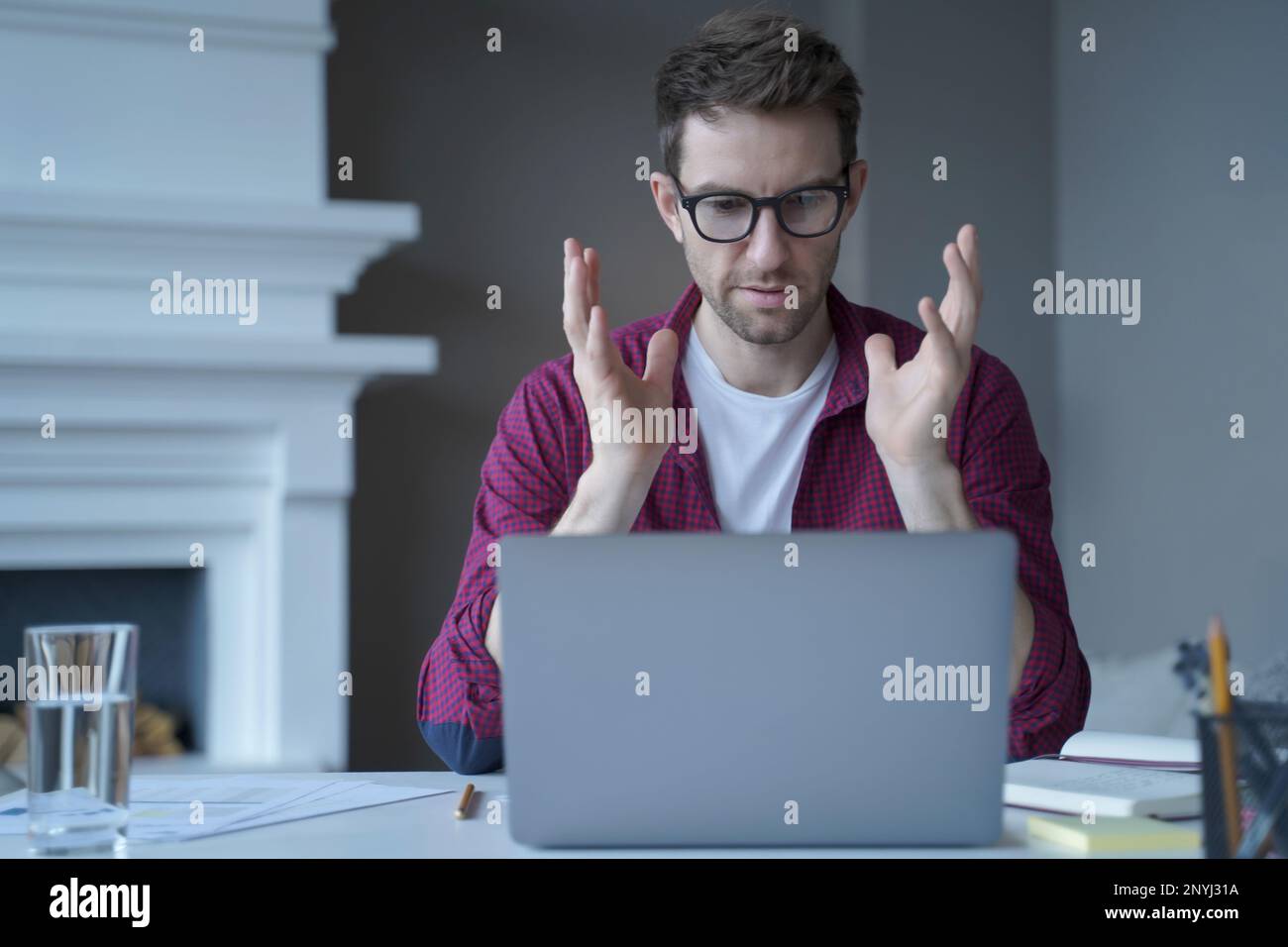Insegnante online uomo serio e concentrato che guarda lo schermo del notebook e parla mentre lavora a distanza da casa, vestito con abiti casual. E-learning Foto Stock