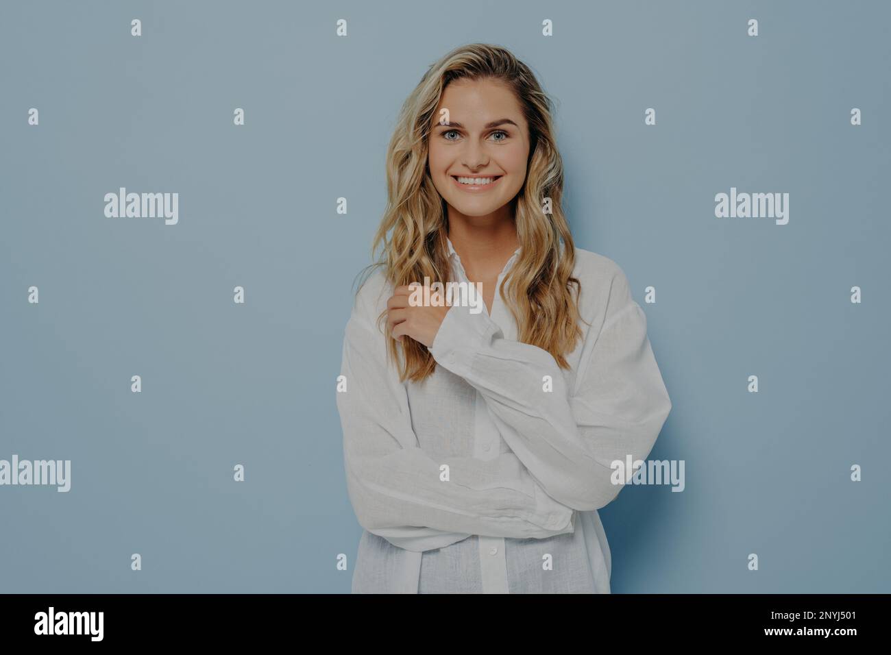 Positivo giovane allegra bella donna con i capelli mossi in abiti casual sorridendo sinceramente alla macchina fotografica, posando con le mani piegate, una mano che tocca Foto Stock