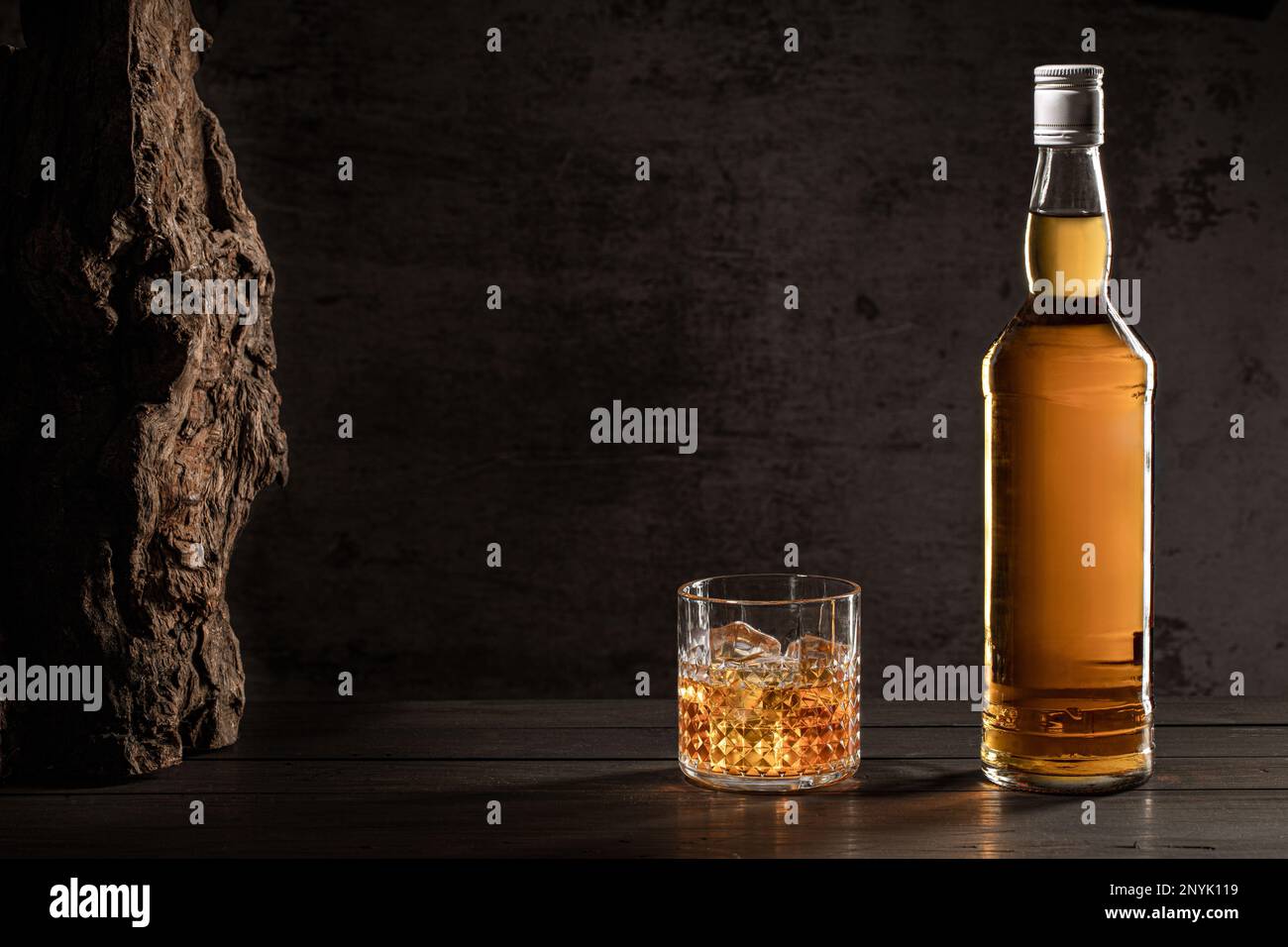 Bottiglia di whisky e vetro con ghiaccio su tavolo di legno con fondo scuro con spazio copia. Foto Stock