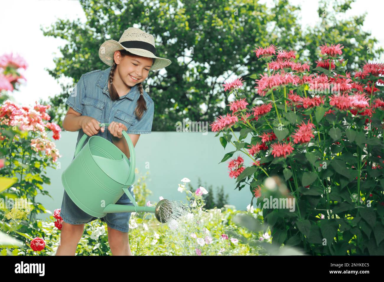 Ragazza felice innaffiando fiori in bel giardino Foto Stock