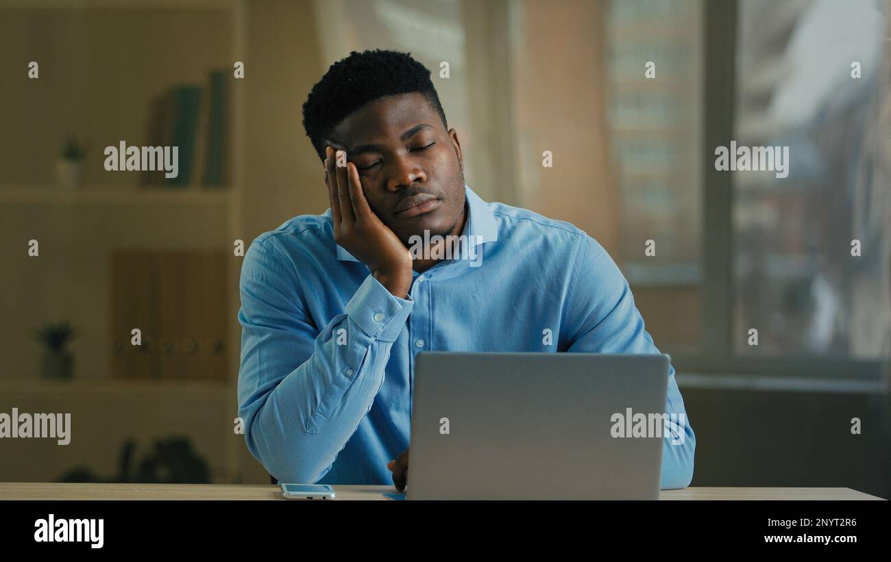 Annoiato stanco esaurito uomo d'affari afroamericano dipendente manager adulto etnia uomo dormire in ufficio nap alla scrivania pigro lavoratore sveglia mobile risposta Foto Stock