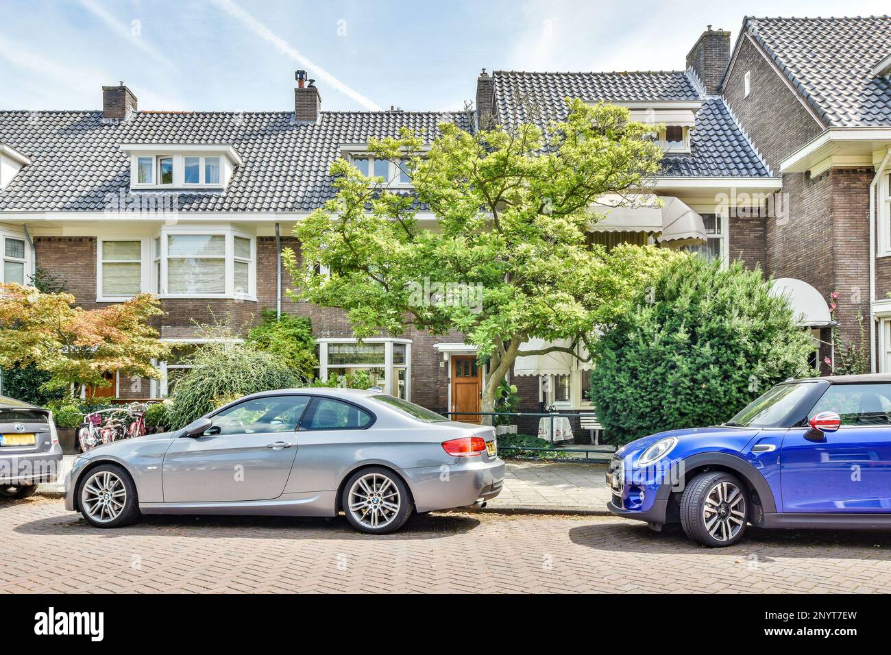 Amsterdam, Paesi Bassi - 10 aprile, 2021: Due auto parcheggiate di fronte a una fila di case in una giornata di sole con cielo blu e nuvole bianche foto stock Foto Stock