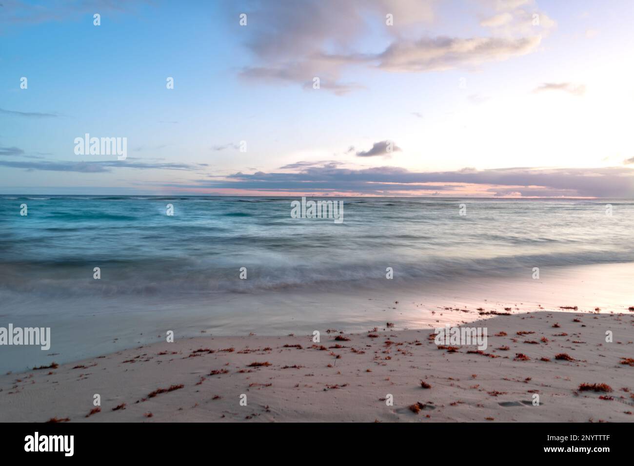 Lunga esposizione di un tramonto color pastello con tranquille onde turchesi che si lavano su una spiaggia delle Barbados. Foto Stock