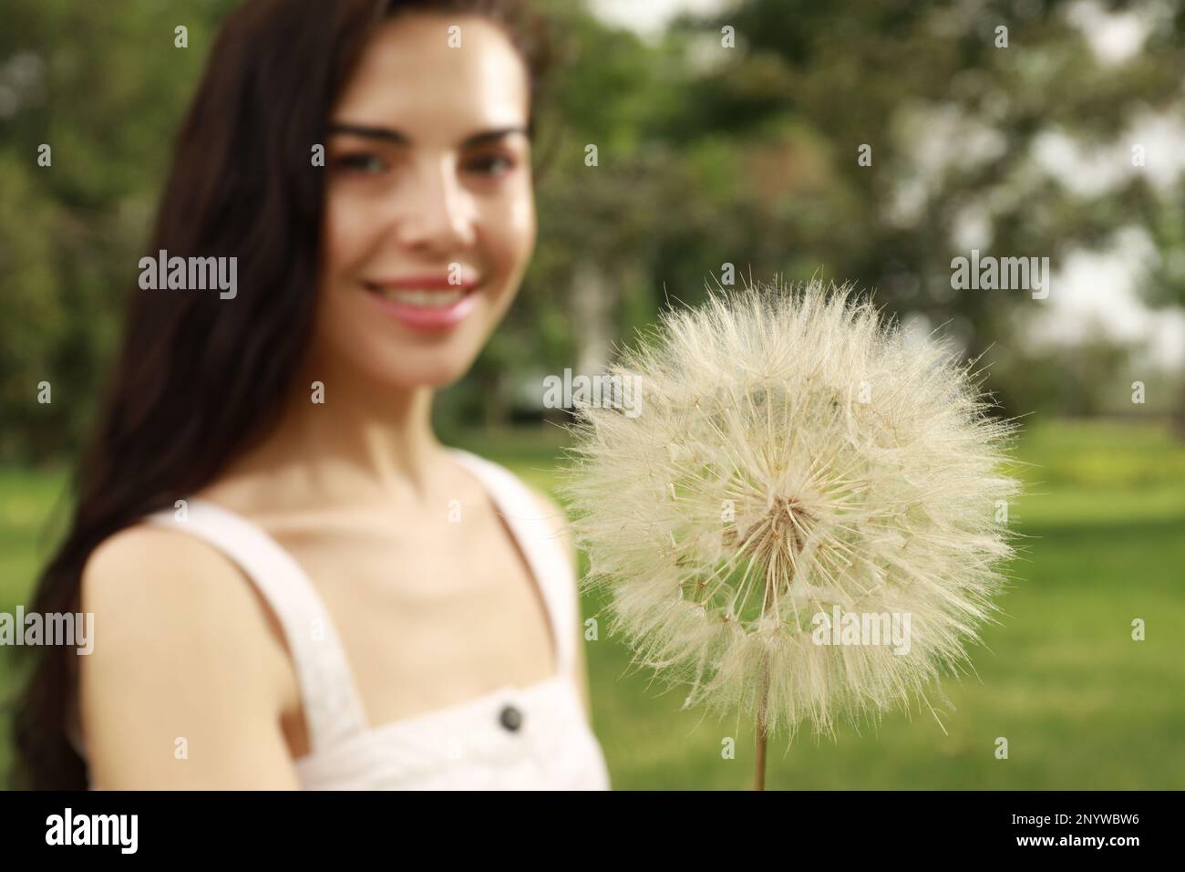 Bella giovane donna con grande dente di leone nel parco, fuoco sul fiore. Concetto di allergia libera Foto Stock