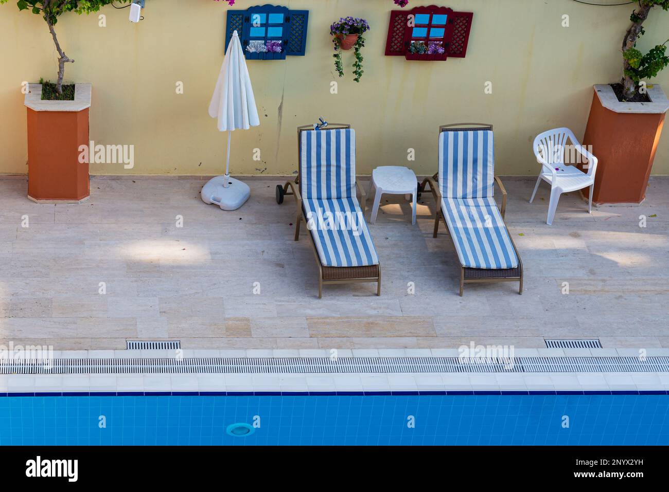Lettini con materassi a strisce sul bordo della piscina con acqua pulita. Foto Stock