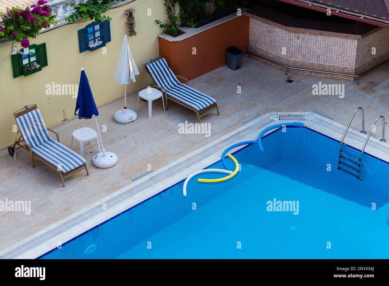 Due lettini con materassi a strisce sul bordo della piscina con acqua pulita. Foto Stock