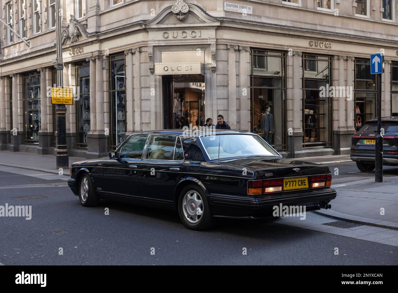 L'auto di lusso Bentley passa davanti alla boutique di moda Gucci su Old Bond Street, Londra, Inghilterra, Regno Unito Foto Stock