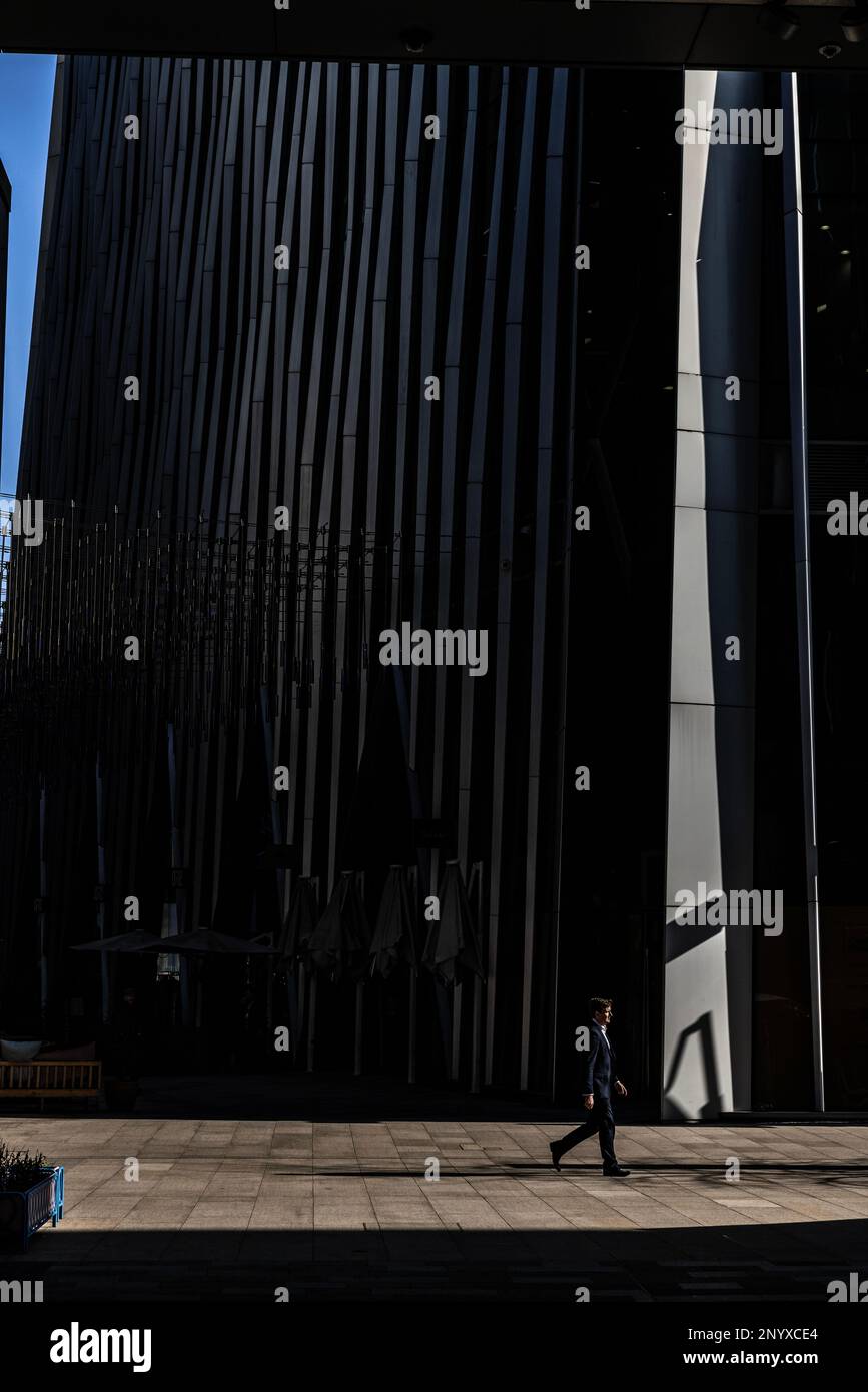 L'operaio della città cammina al sole di mezzogiorno accanto a un alto edificio nella City of London, England, United Kingdom Foto Stock