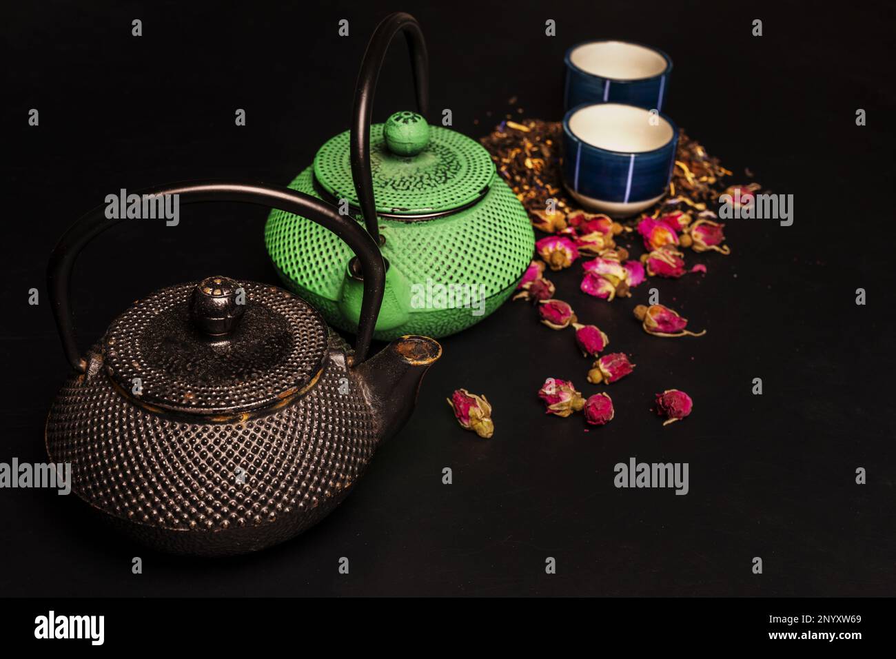 Un paio di teiere in ghisa con alcune piccole tazze di porcellana e tè di rosa essiccato Foto Stock