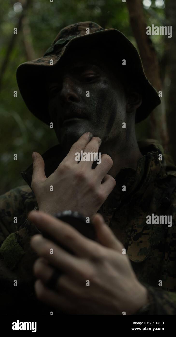 STATI UNITI Nicholas Chrastil, un fucile con 1st battaglione, 7th Marines, applica la pittura mimetizzazione della faccia durante l'esercizio 23 di Jungle Warfare nella zona di addestramento del Nord a Okinawa, Giappone, 14 febbraio 2023. JWX 23 è un'esercitazione di formazione sul campo su larga scala incentrata sull'utilizzo delle capacità integrate di partner congiunti e alleati per rafforzare la consapevolezza, la manovra e gli incendi in tutti i settori in un ambiente marittimo distribuito. Chrastil è un nativo di Creta, Nebraska. Foto Stock