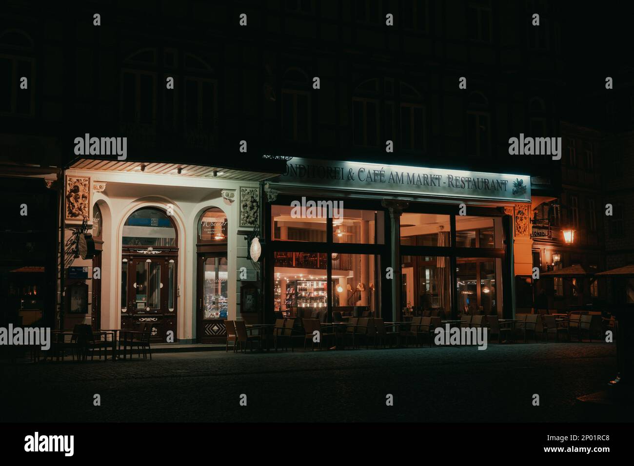 Un ristorante e' mostrato dall'esterno di notte. All'interno le luci sono accese e all'esterno ci sono delle sedie. Il ristorante si trova in una Germania. Foto Stock