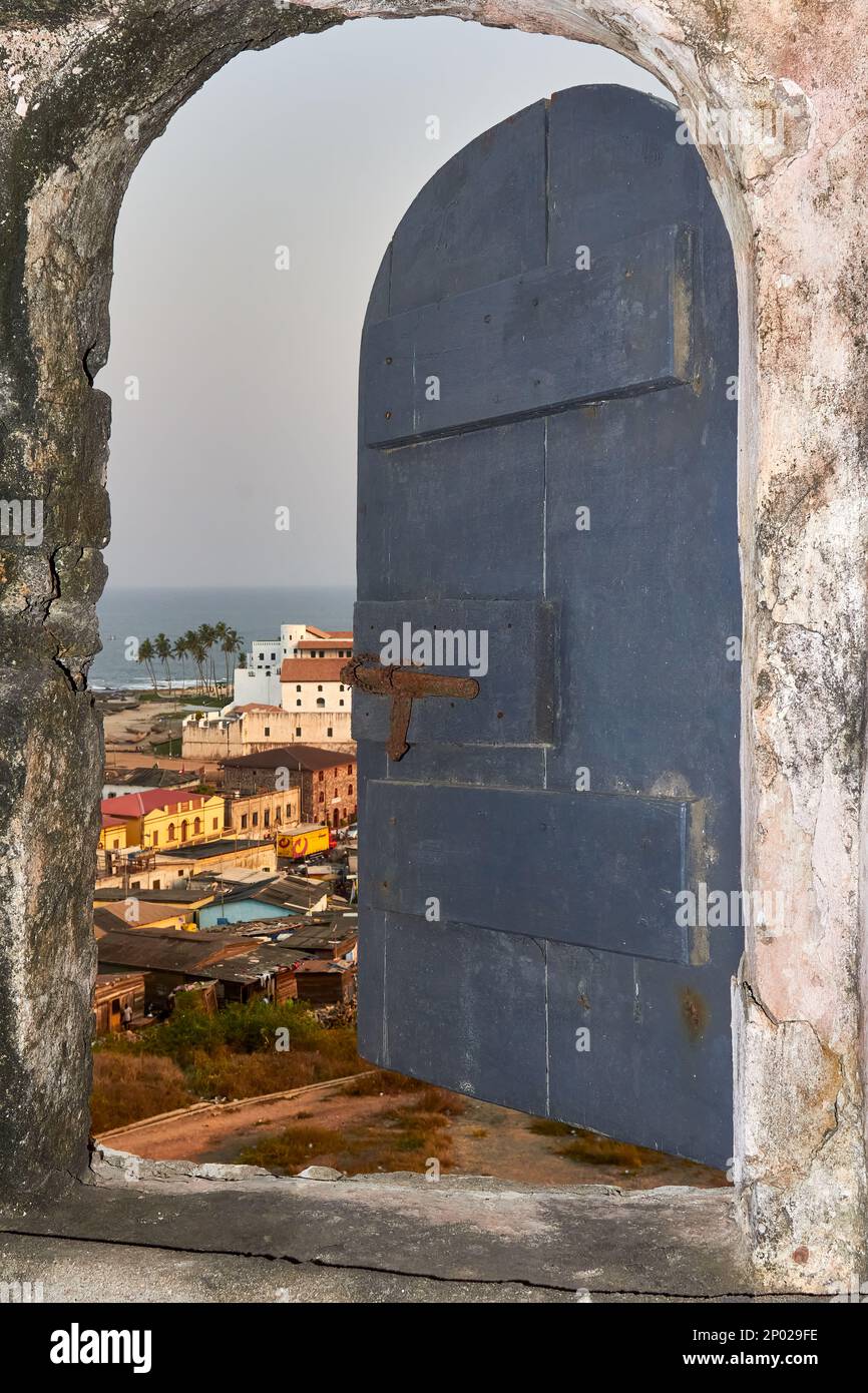 Vista degli edifici e del mare attraverso una finestra di pietra al Castello di Elmina, Elmina, Ghana Foto Stock