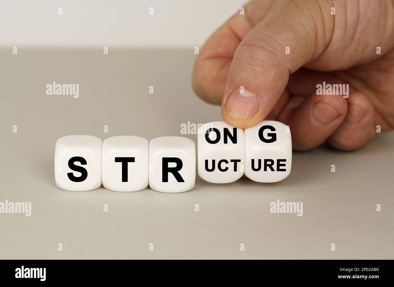 Su una superficie grigia sono presenti cubi bianchi con l'iscrizione - FORTE o STRUTTURA. Due dadi in mano. Concetto aziendale. Foto Stock