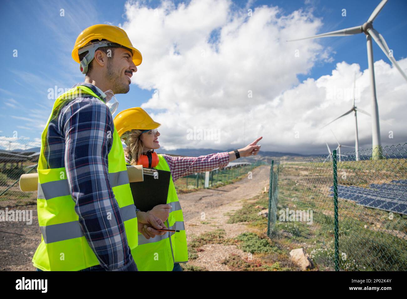 Due ingegneri stanno tenendo una conversazione mentre osservano le turbine eoliche, il concetto di energia rinnovabile. Foto Stock Due ingegneri stanno tenendo una conversazione mentre osservano le turbine eoliche, il concetto di energia rinnovabile. Foto Stock