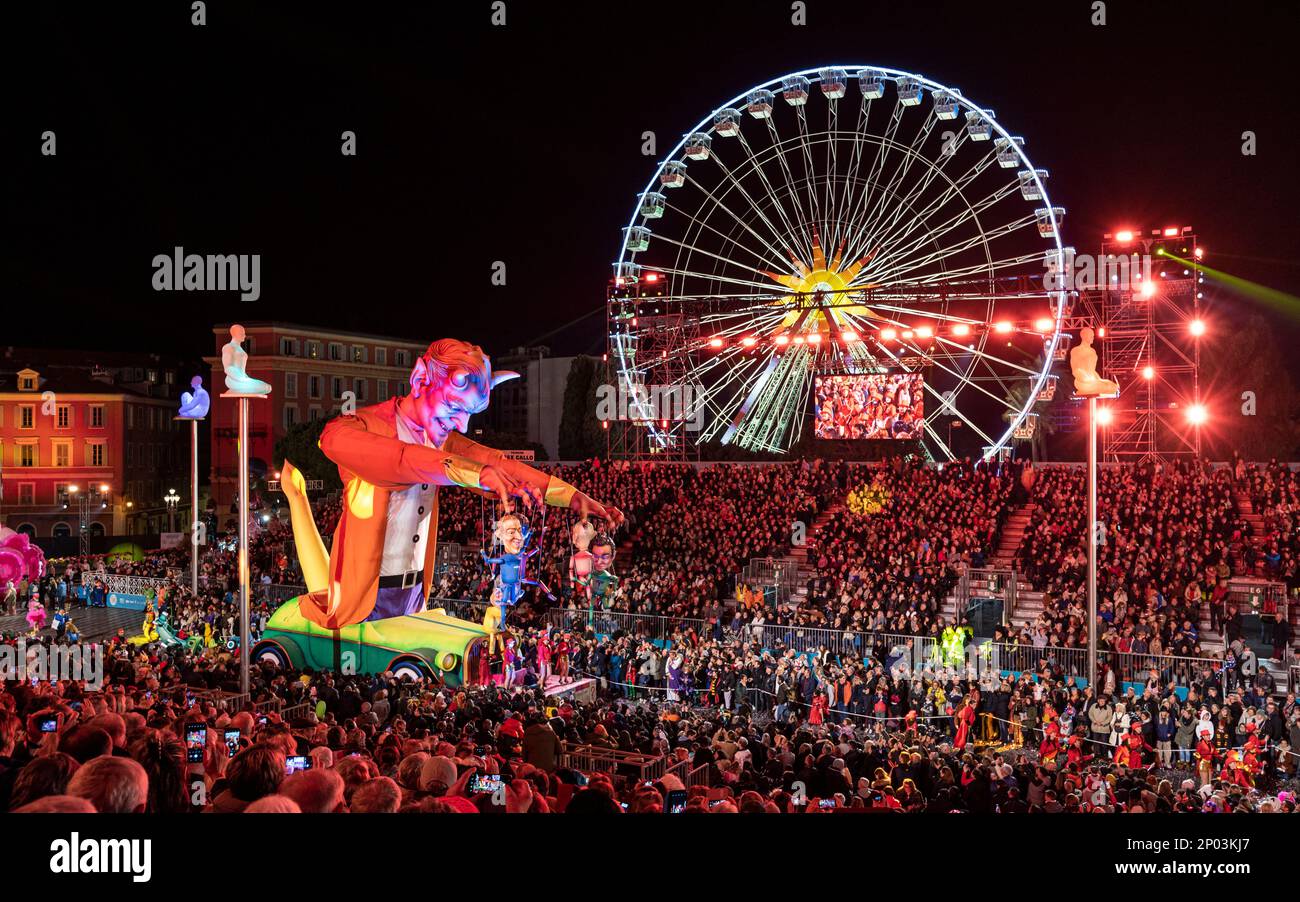 Galleggia di notte (burattino del Maestro del Diavolo) alla parata annuale di luci del Carnevale 150th a Nizza. Grande ruota panoramica sullo sfondo. Foto Stock