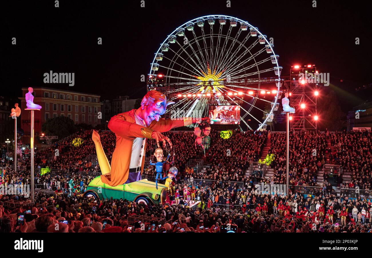Galleggia di notte (burattino del Maestro del Diavolo) alla parata annuale di luci del Carnevale 150th a Nizza. Grande ruota panoramica sullo sfondo. Foto Stock