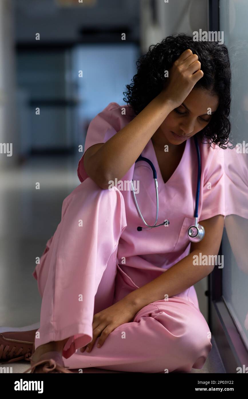 Medico di sesso femminile biraciale esausto con uno stetoscopio appoggiato alla porta in ospedale Foto Stock