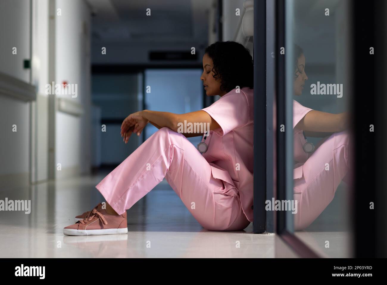 Medico di sesso femminile biraciale esausto con uno stetoscopio appoggiato alla porta in ospedale Foto Stock