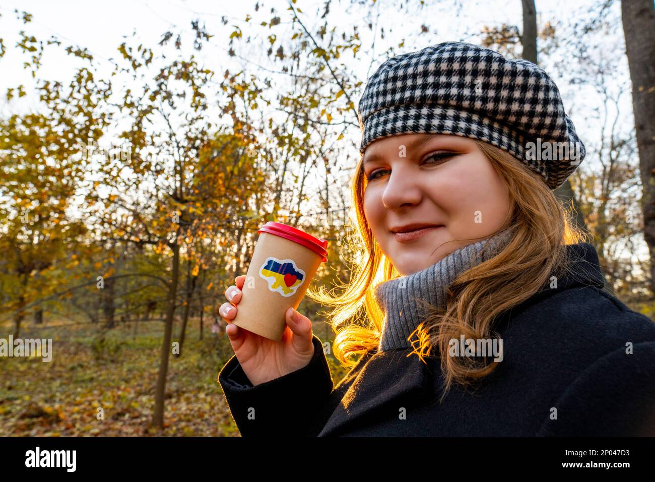 Ucraina. Tramonto. Parco cittadino. Fine giornata lavorativa. La ragazza tiene in mano la tazza di caffè con un adesivo patriottico 'Io amo l'Ucraina'. Passeggiate all'aria aperta Foto Stock