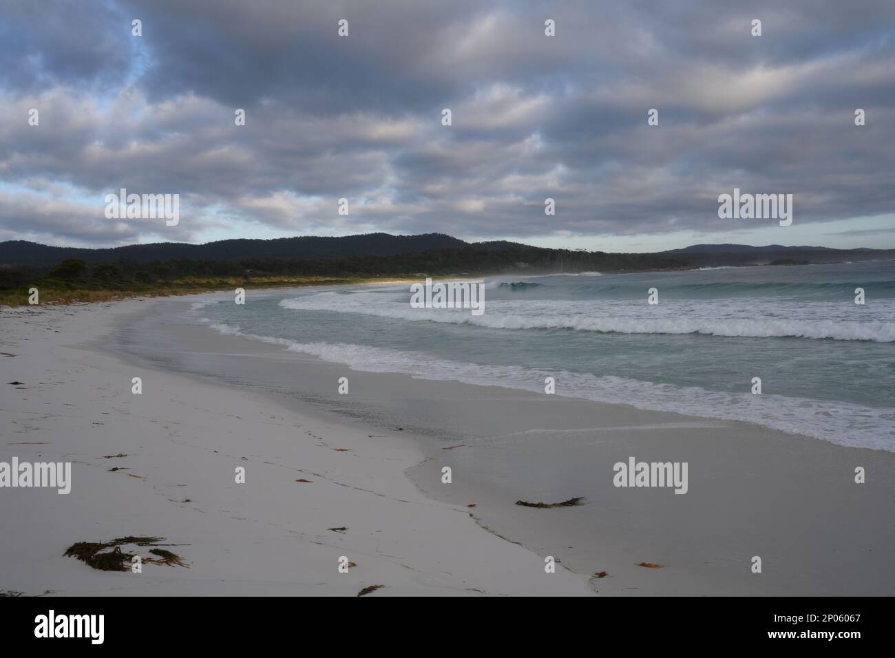 Le nuvole del mattino presto sono appese nell'aria ferma mentre una matrice di coperte il cielo sopra una spiaggia e le onde che si infrangono Foto Stock