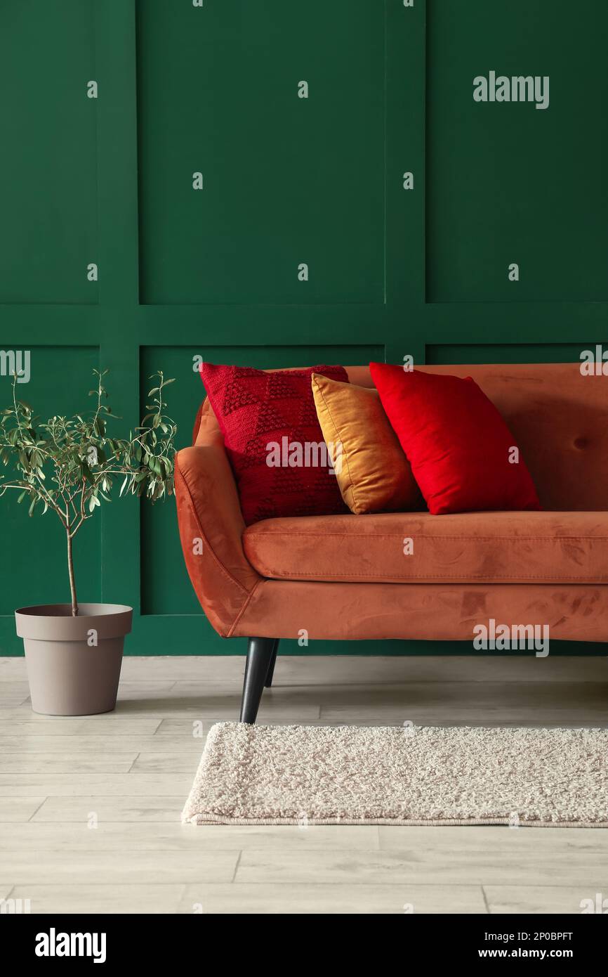 Divano rosso con eleganti cuscini e piante vicino al muro verde Foto Stock