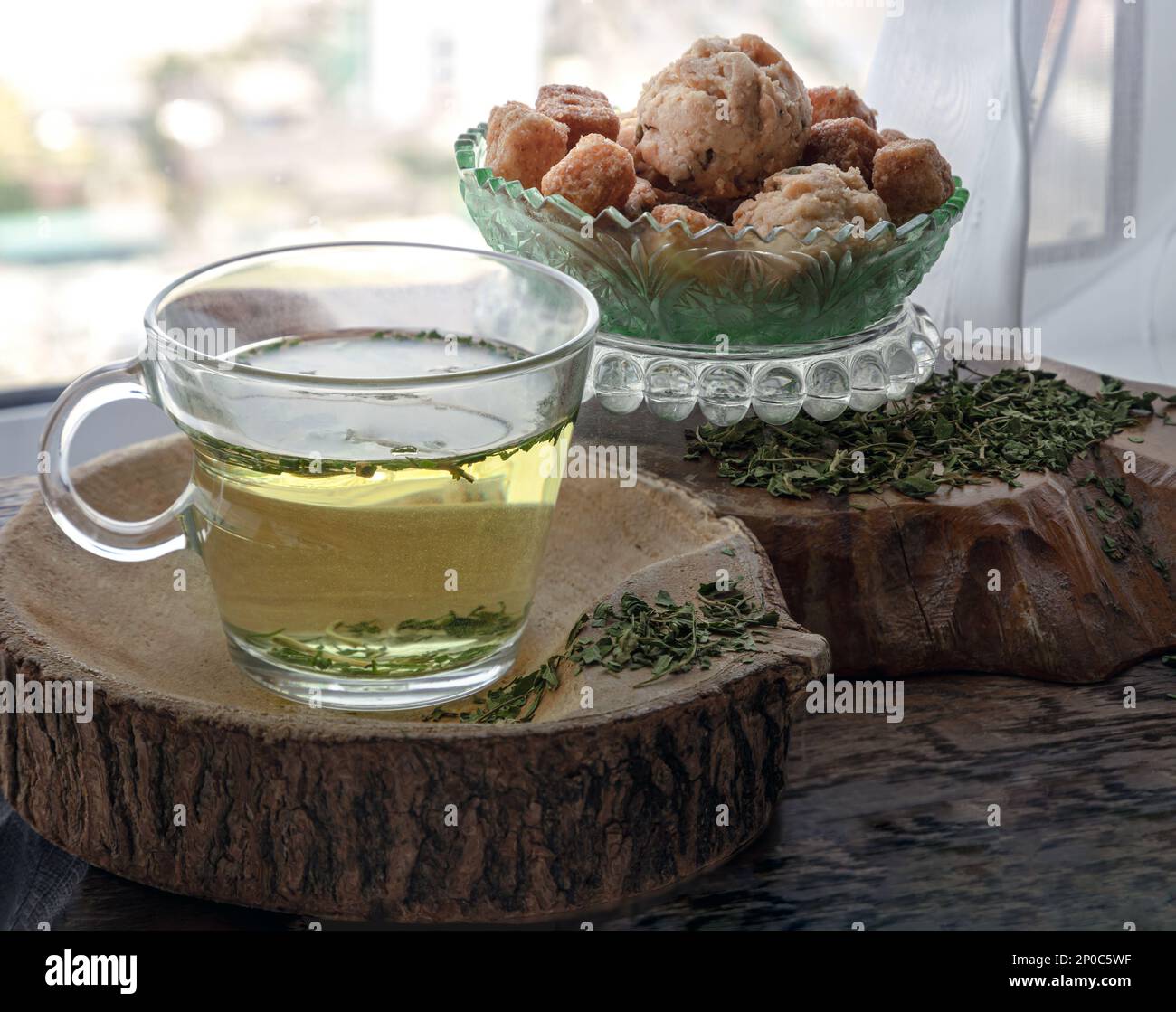 Rinfrescati e gusta una tazza di tè alla canapa calda (tè alle erbe del CBD) servito con focaccine e crostini su un vecchio tavolo rustico in legno vicino alla finestra con su Foto Stock