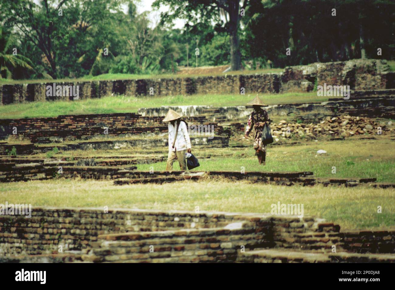 Agricoltori che camminano attraverso le rovine del Palazzo Surosowan, un patrimonio culturale del periodo Sultanato Banten situato in un'area chiamata Banten lama (Old Banten) a Serang, Banten, Indonesia, in questa foto scattata nel 2004. Una ricerca sul campo condotta recentemente da Nurikah e E. Rakhmat Jazuli (Facoltà di giurisprudenza, Sultan Ageng Tirtayasa University, Banten) ha rivelato che ci sono state molte violazioni contro il trattamento dei beni culturali nella zona. Foto Stock