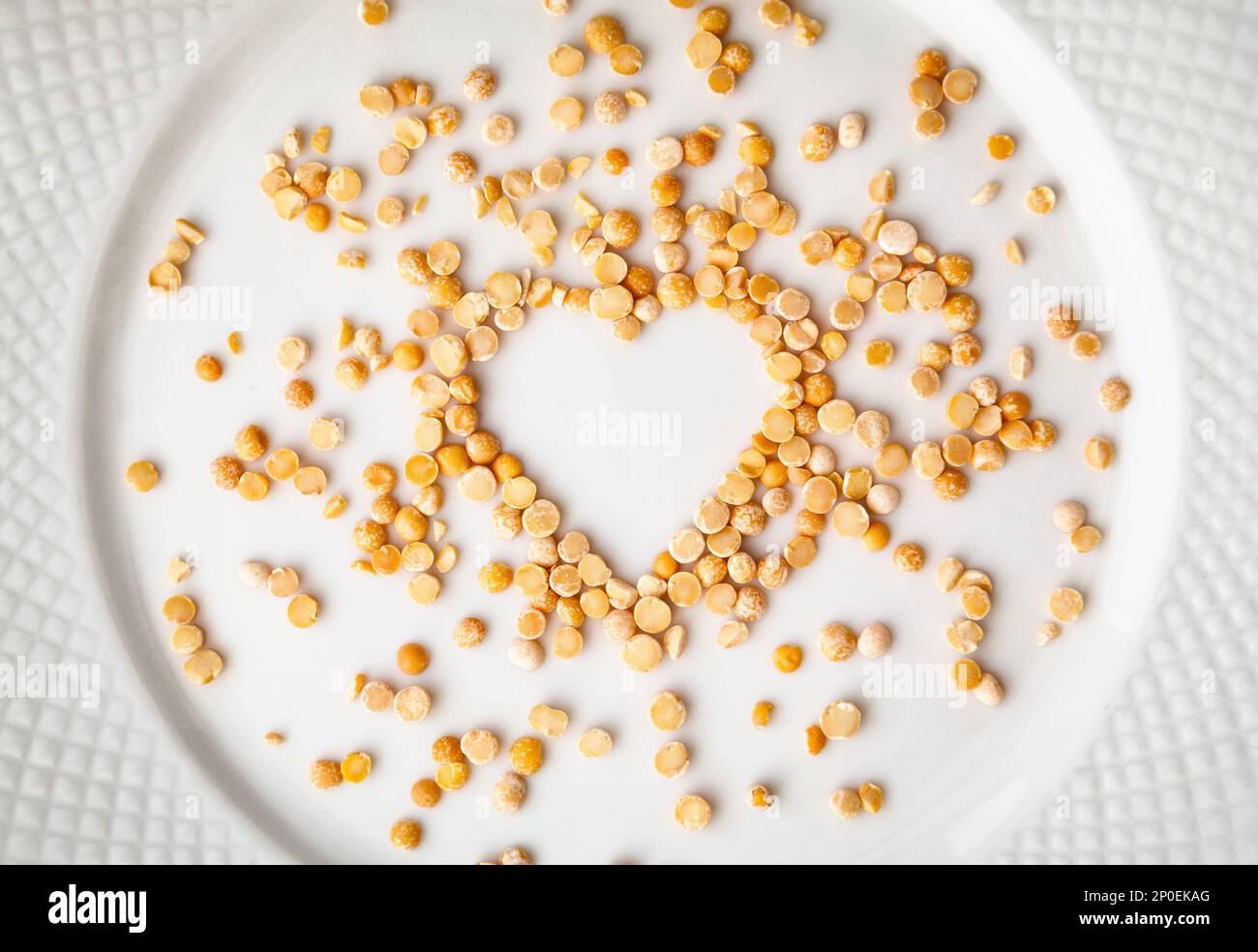 Piselli secchi gialli a forma di cuore versati su un piatto bianco. Groats crudo ingrediente di fondo. Amore per il concetto di cucina Foto Stock
