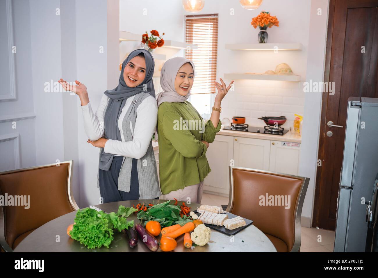 due donne in hijab con gesto della mano che si presenta durante la cottura Foto Stock