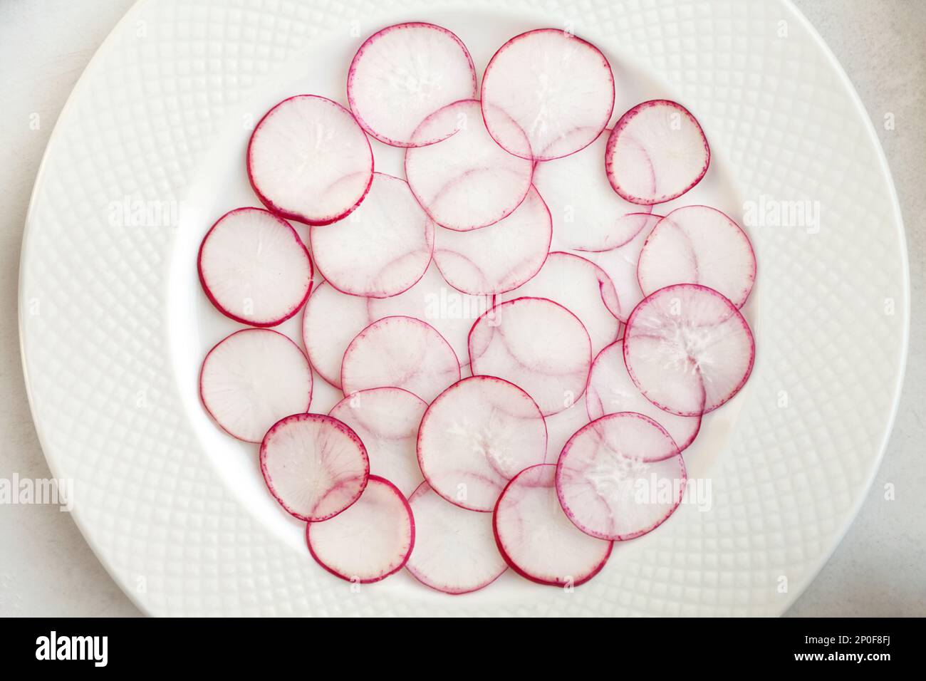 Sacco di rafano sottili fette sovrapposte su una piastra bianca dello sfondo. Rossa affettata ingrediente di rafano per insalata. Bellissimi ambienti vegetali pattern Foto Stock