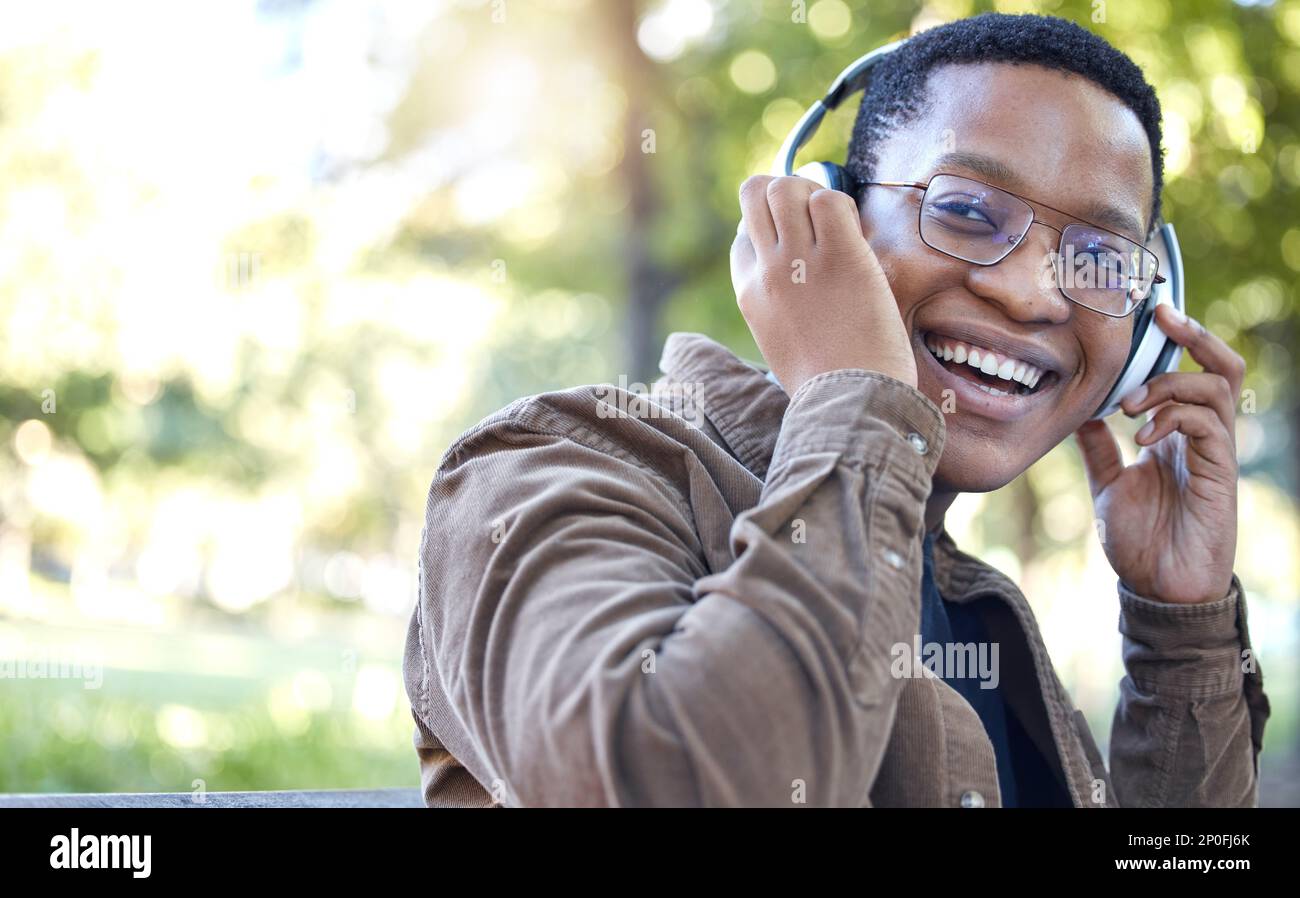 Cuffie, parco e ritratto di uomo nero che ascolta musica per esterni, salute mentale e rilassante pausa nella natura. Giovane studente africano o felice Foto Stock