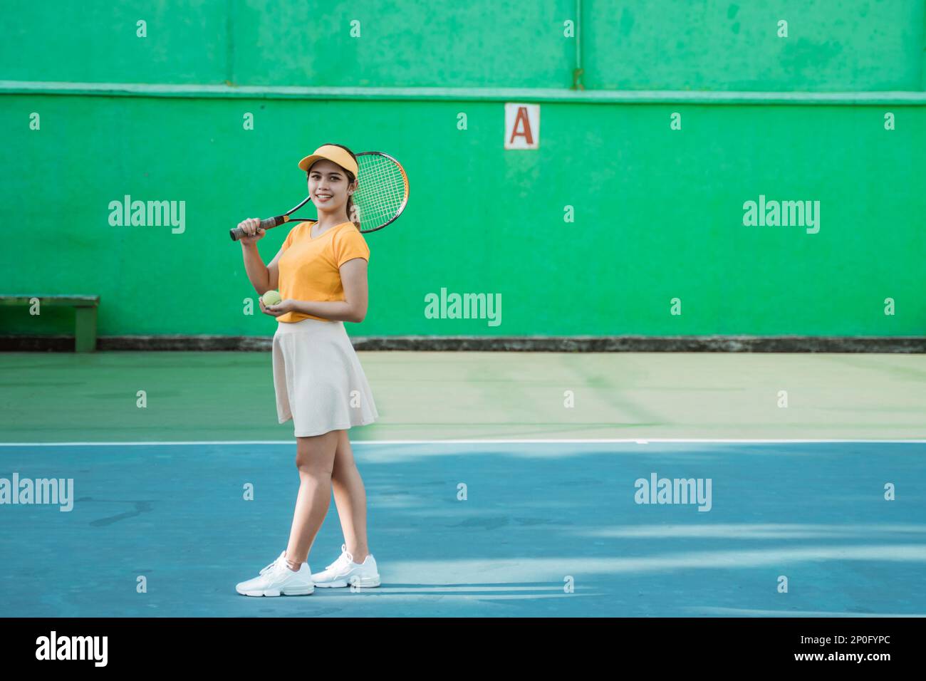 Sorridente tennista che porta racchetta e palla sul campo da tennis Foto Stock