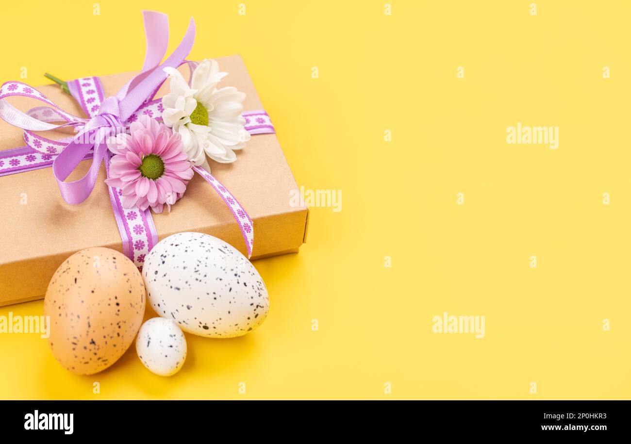 Confezione regalo, uova di Pasqua e fiori su sfondo giallo con spazio per i vostri saluti Foto Stock