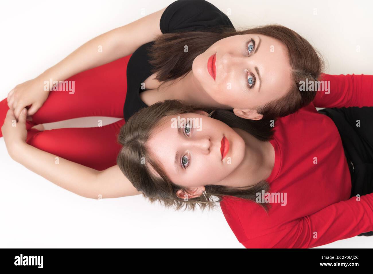 Vista dall'alto di mamma e figlia seduti con le spalle l'una all'altra e mettere la testa sulle spalle dell'altra. Entrambe le donne che guardano in alto la macchina fotografica Foto Stock