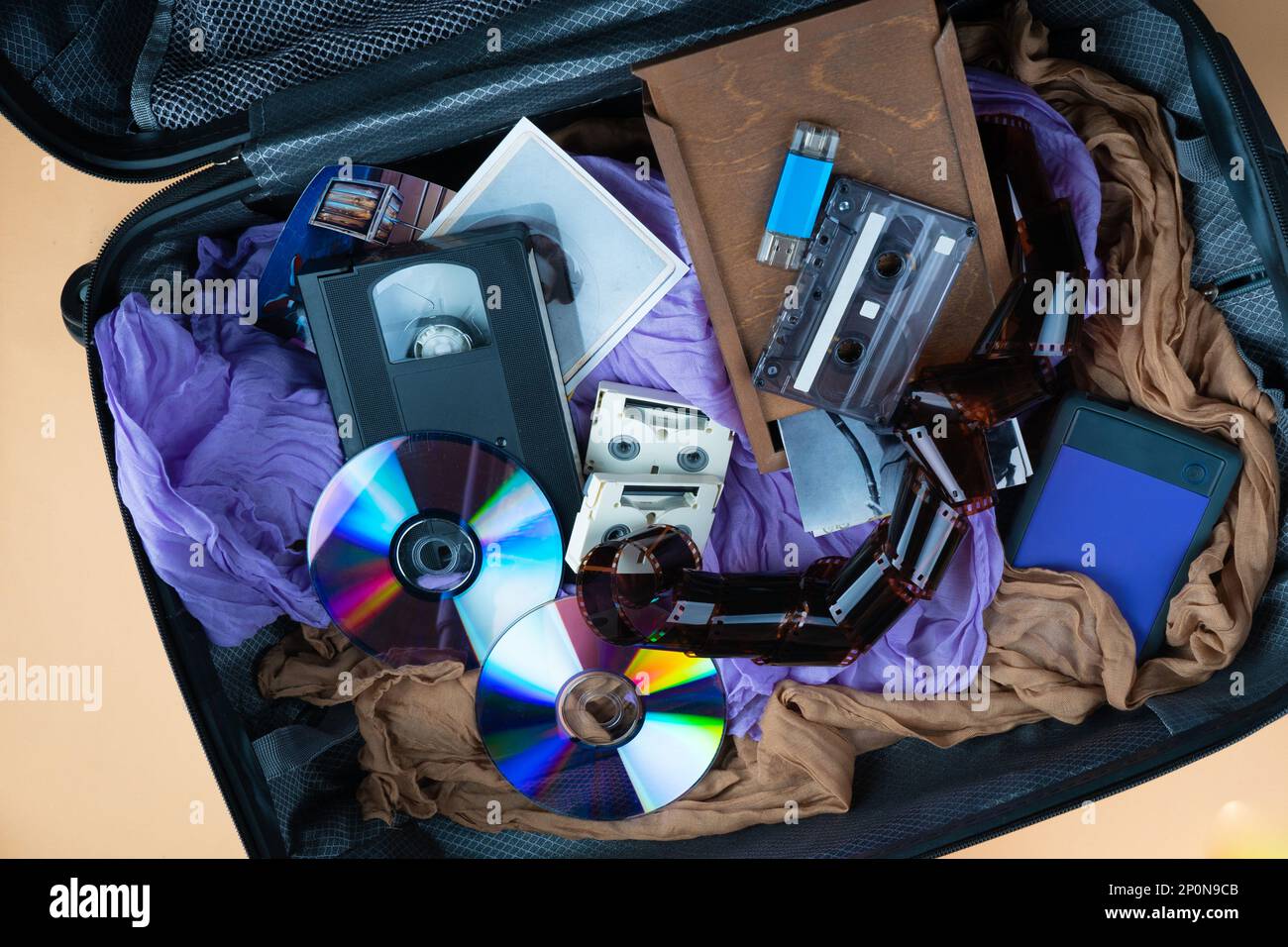 Più dispositivi di stoccaggio moderni e retrò nella valigia. Ricordi di famiglia su diverse cassette, pendrive, hdd, schede di memoria, dischi USB esterni. Vista dall'alto. Foto Stock