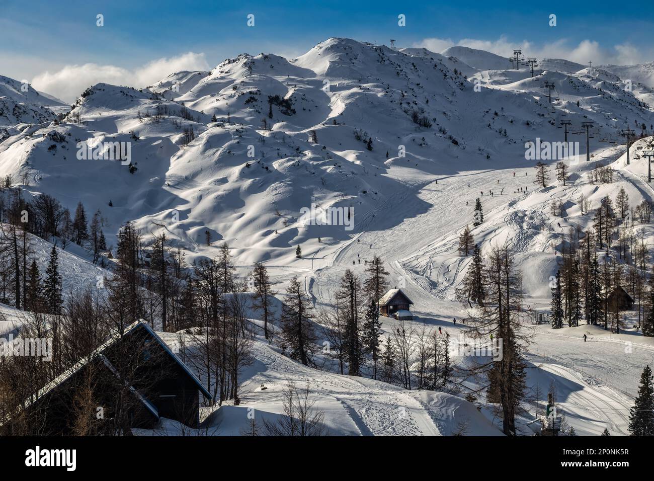 Bohinj, Slovenia - Vista invernale della montagna innevata Vogel con sciatori sulle piste da sci e capanne in legno nelle Alpi nel Parco Nazionale del Triglav su una collina soleggiata Foto Stock
