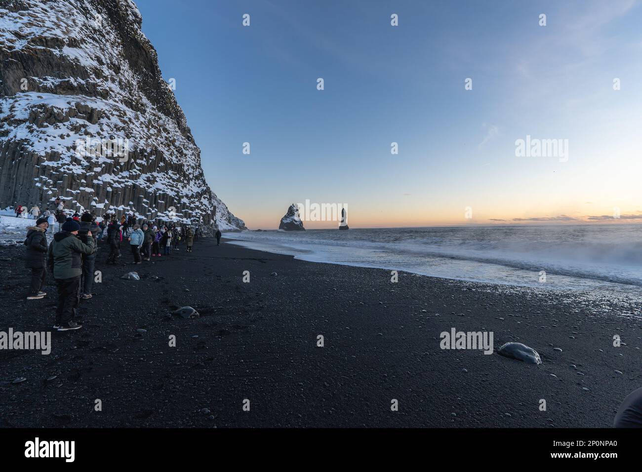 Reynisfjara spiaggia di sabbia nera al tramonto illuminata dagli ultimi raggi del sole dall'orizzonte del mare con turisti stupiti e scattando foto Foto Stock