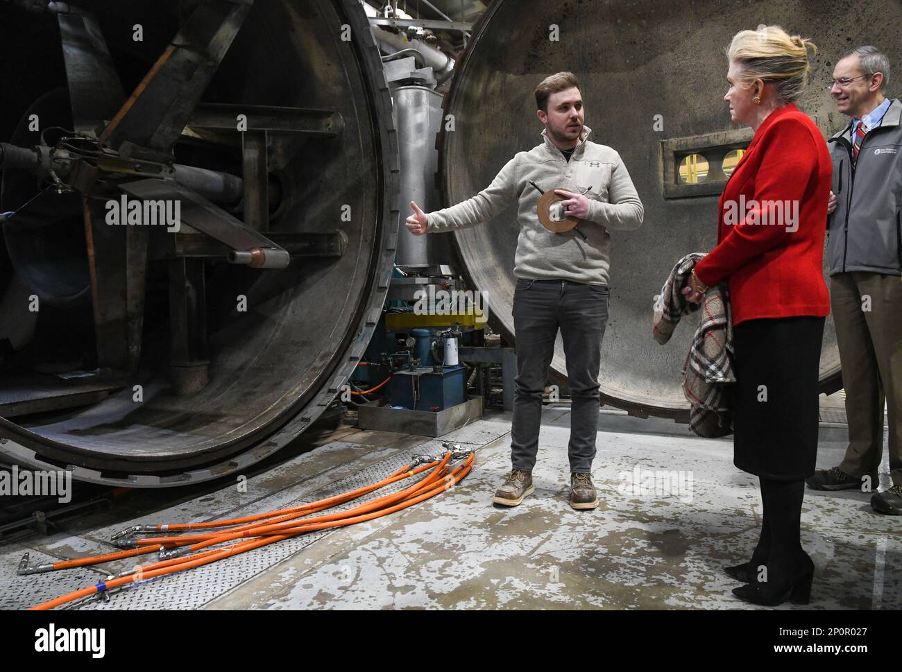 Cooper Green, un ingegnere di test degli archi, parla del sistema di posizionamento dei modelli, visto a sinistra, al Sen. Marsha Blackburn durante la sua visita alla base dell'aeronautica militare di Arnold, Tennessee, sede del Arnold Engineering Development Complex, 27 gennaio 2023. Il verde contiene uno dei segmenti che compongono un riscaldatore ad arco, che crea essenzialmente un fulmine controllato in un tubo allo scopo di testare materiali sottoposti a calore e forze di taglio estreme. Il sistema di posizionamento del modello consente al personale di test di ruotare più oggetti di test attraverso il flusso del getto d'arco durante una sessione di test. Foto Stock