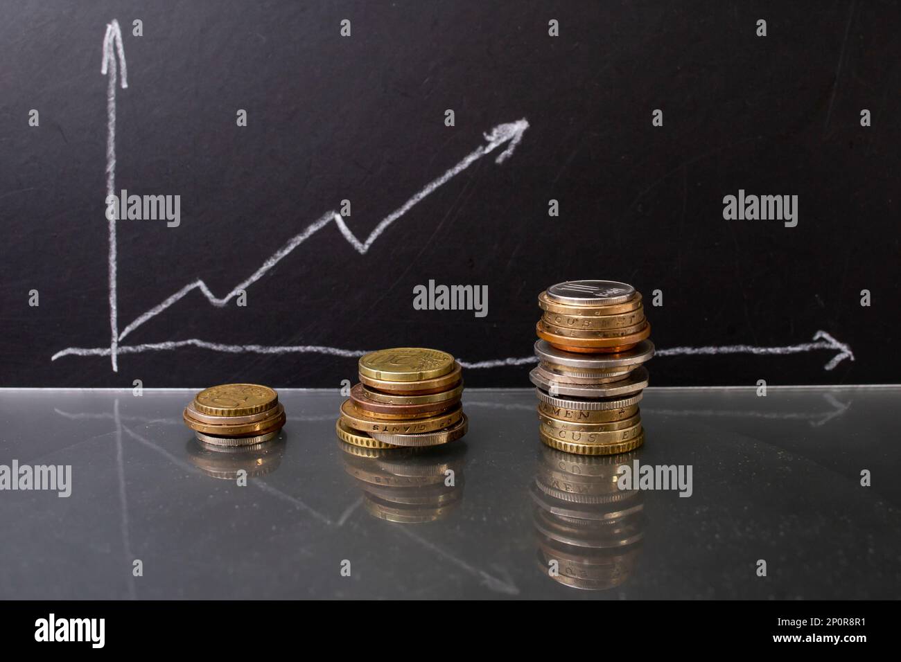 Pile di monete accanto a un grafico ascendente su una tavola di gesso nero. Primo piano Foto Stock