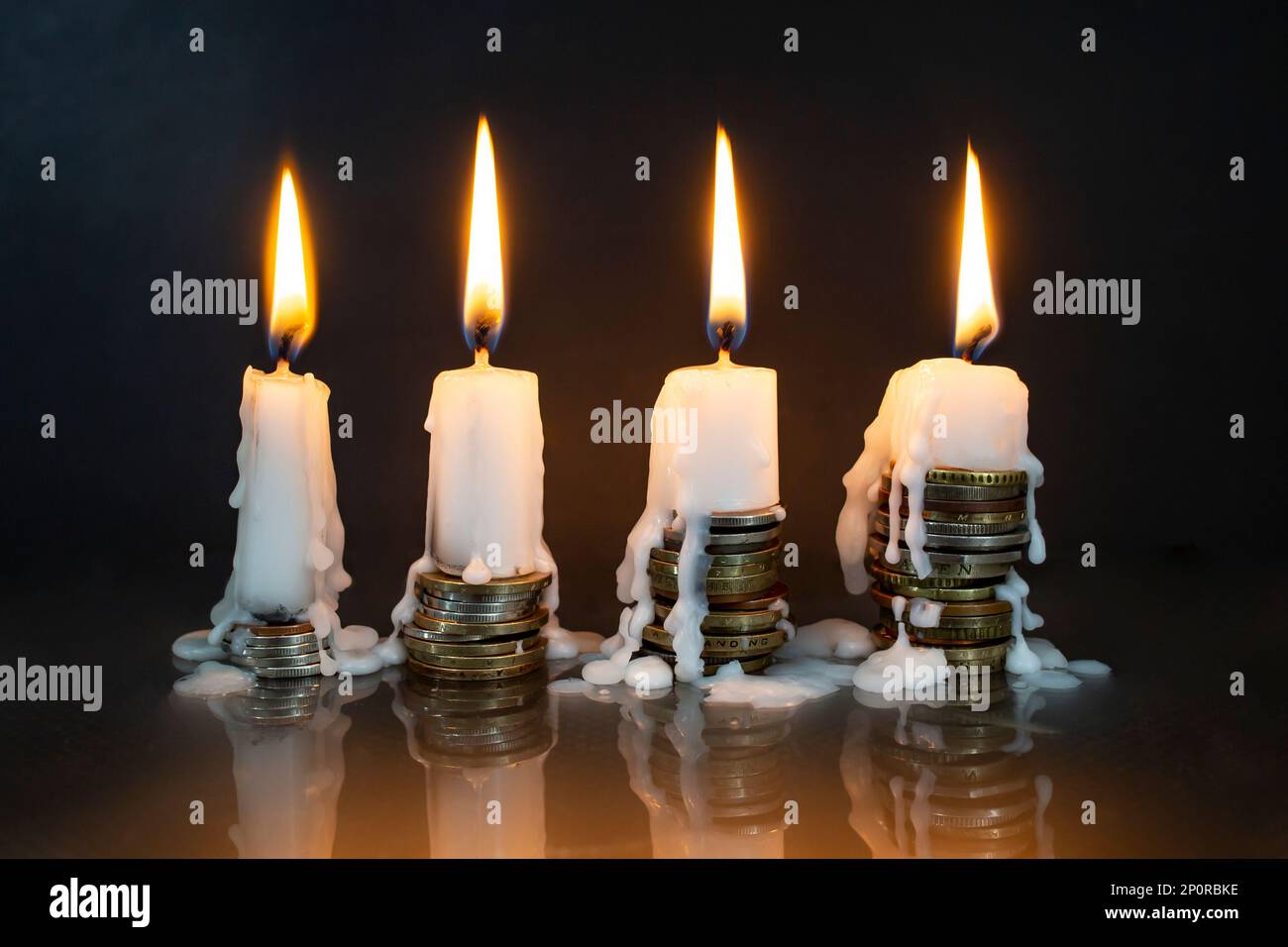 candele bianche che bruciano in cima su pile di monete, su sfondo scuro. Più soldi, meno metafora di vita Foto Stock