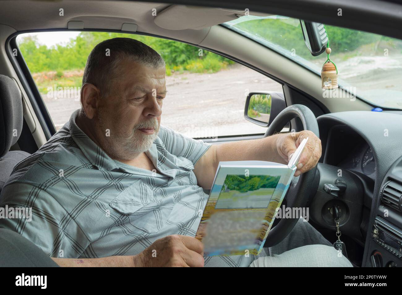 Ritratto di SittiCang anziano ucraino seduto all'interno della sua auto e libro di lettura Foto Stock