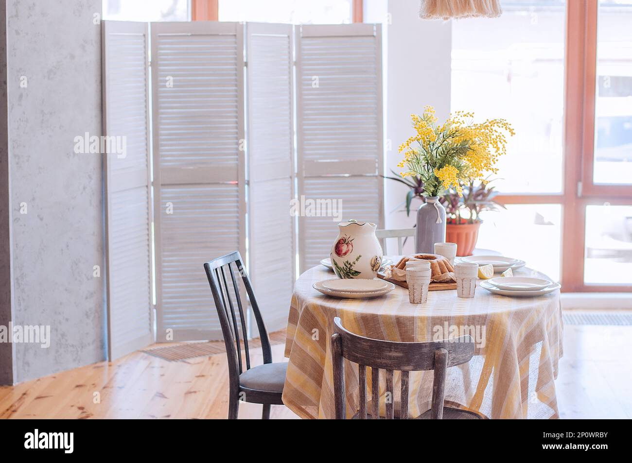 Primavera, Pasqua interni in stile scandinavo. Rustico soggiorno con un luminoso armadio, mimosa giallo in vaso. La tabella viene impostata in modo festivo con ceram Foto Stock