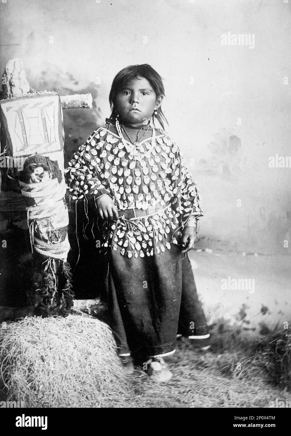 Indiani, americani - Bambini, 1916. Ragazza nativa americana vestito con decorazione applique. L'oggetto a sinistra può essere una tavola da culla con la bambola attaccata. Foto Stock