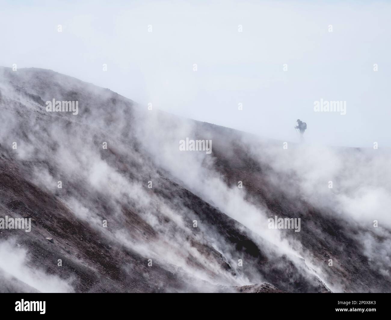 Silhouette di uomo trekking alla coldera di Avachinsky stratovulcano, noto anche come vulcano Avacha. Il turista del Backpacker si muove sulle rocce dietro il vapore Foto Stock