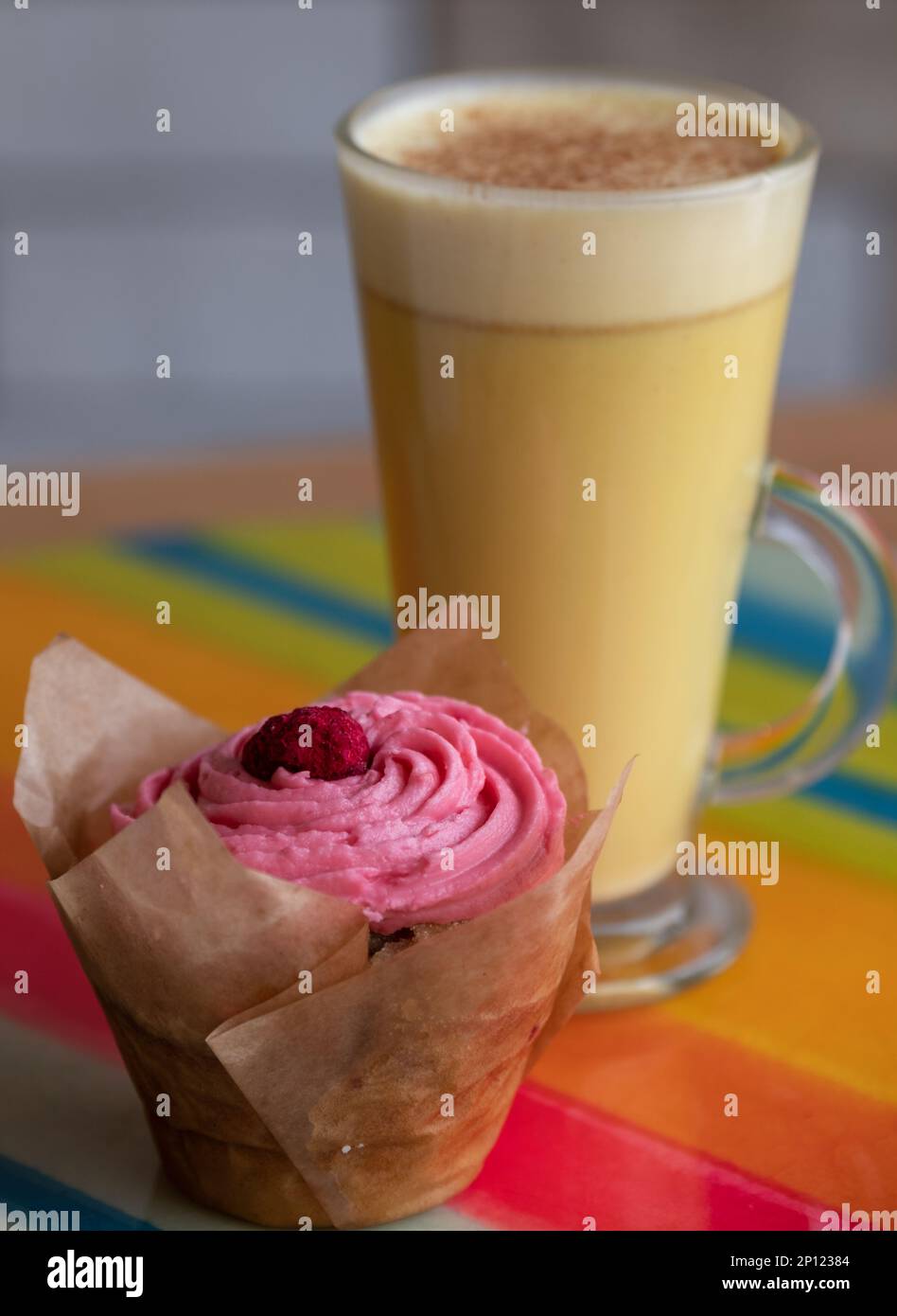 Bicchiere di chai latte fatto con latte vegetale senza latticini, con cupcake vegano con glassa rosa in primo piano. Servito su un piatto colorato. Foto Stock