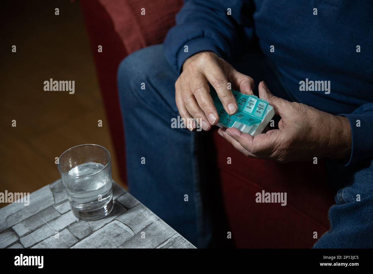 Primo piano delle mani di un Signore anziano che prende le pillole dal suo organizzatore di pillole. Foto Stock