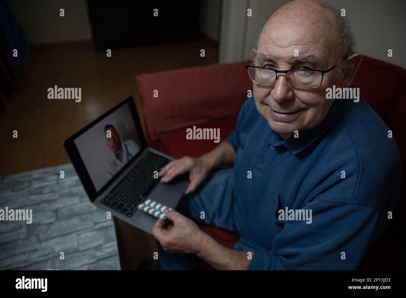 Ritratto di un uomo anziano durante una videochiamata con il suo medico generico che tiene il computer portatile e le pillole Foto Stock