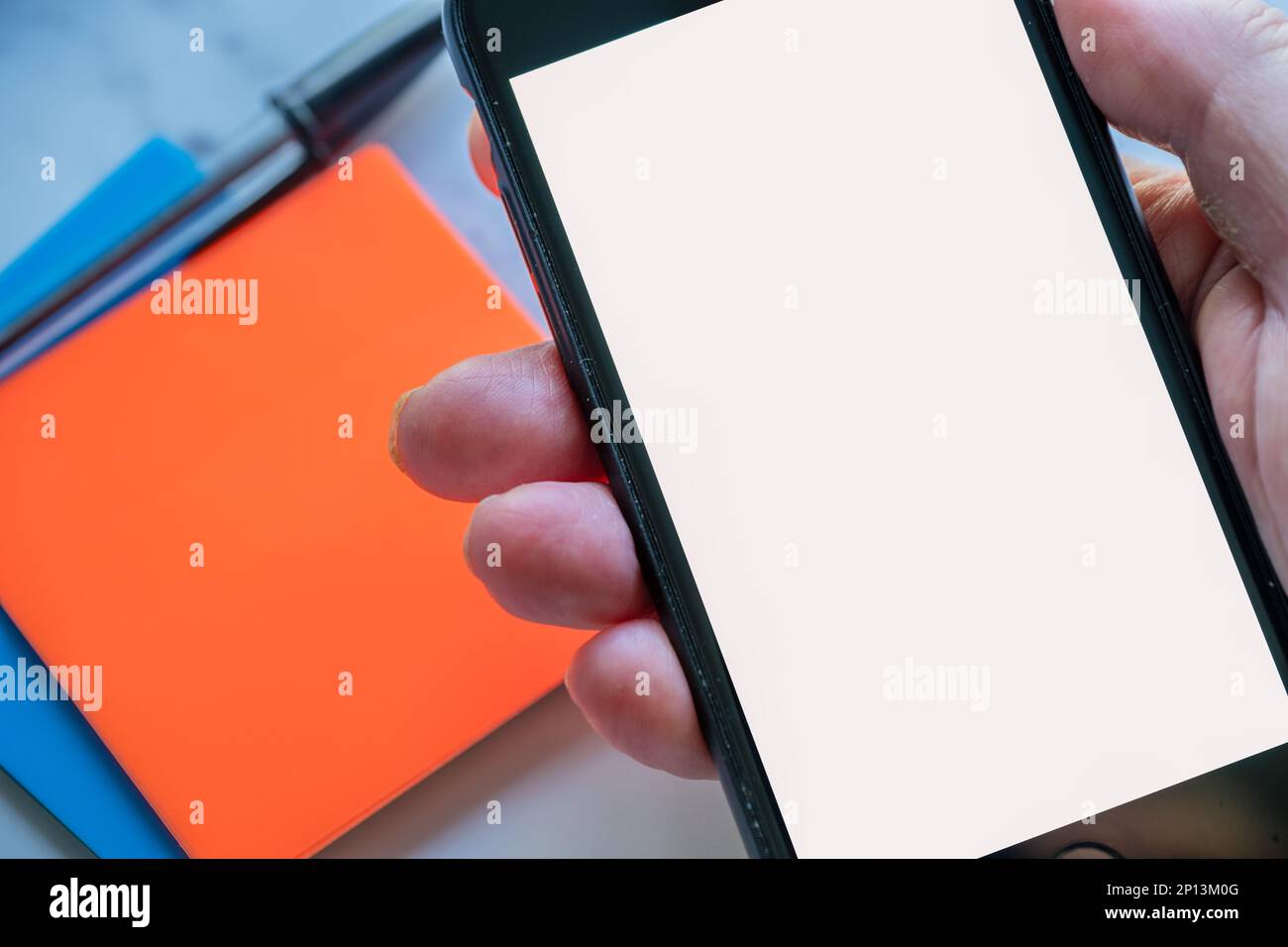 simulazione di una persona che tiene in mano uno smartphone con schermo vuoto e ufficio fisso nella vista ravvicinata dello sfondo Foto Stock