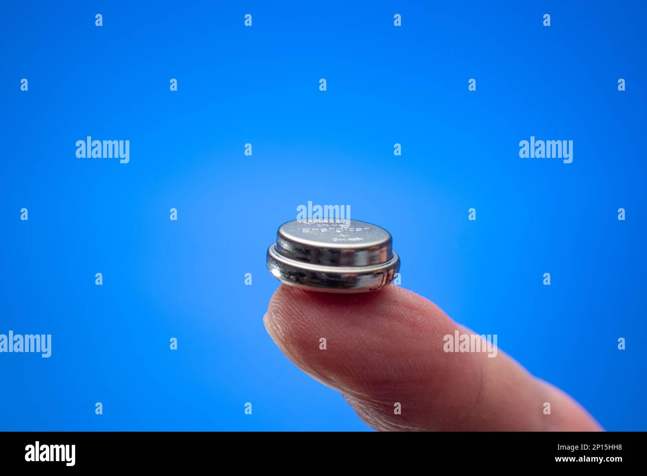 Mano maschio caucasica che tiene una batteria a bottone tra le dita. Primo piano ripresa in studio, isolata su sfondo bianco. Foto Stock